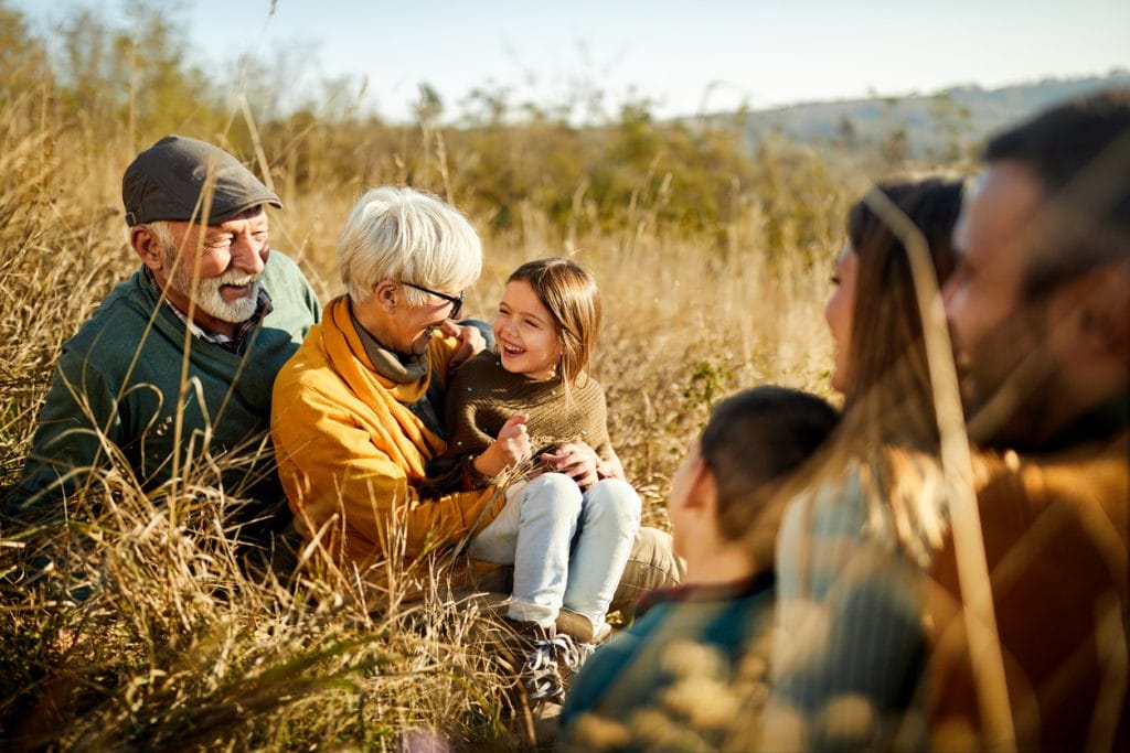 Multi-generational family sat together in a field discussing equity release and alternative options to boost retirement income.
