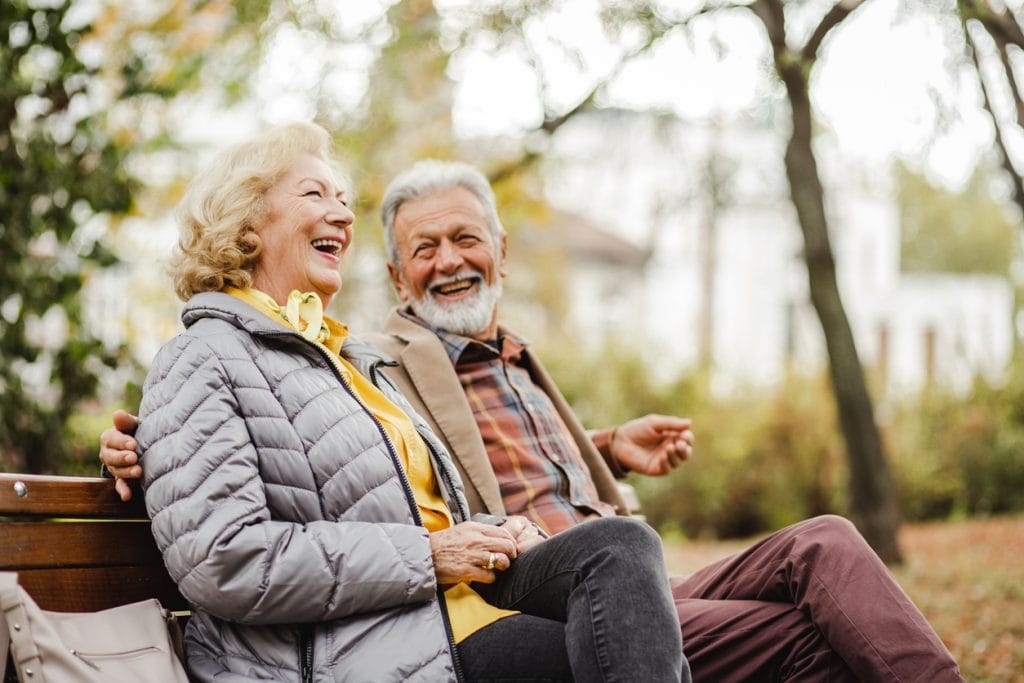 couple sitting together on a park bench enjoying their retirement after using equity release to boost their income.